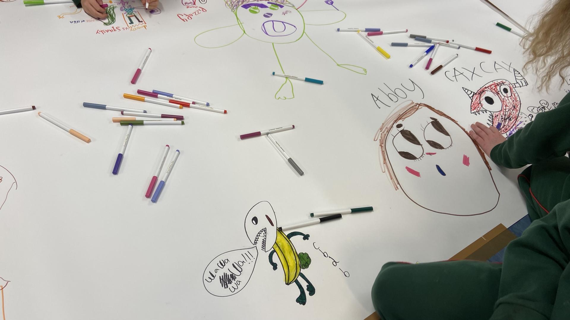 Close-up of colorful character drawings on a large sheet surrounded by markers.