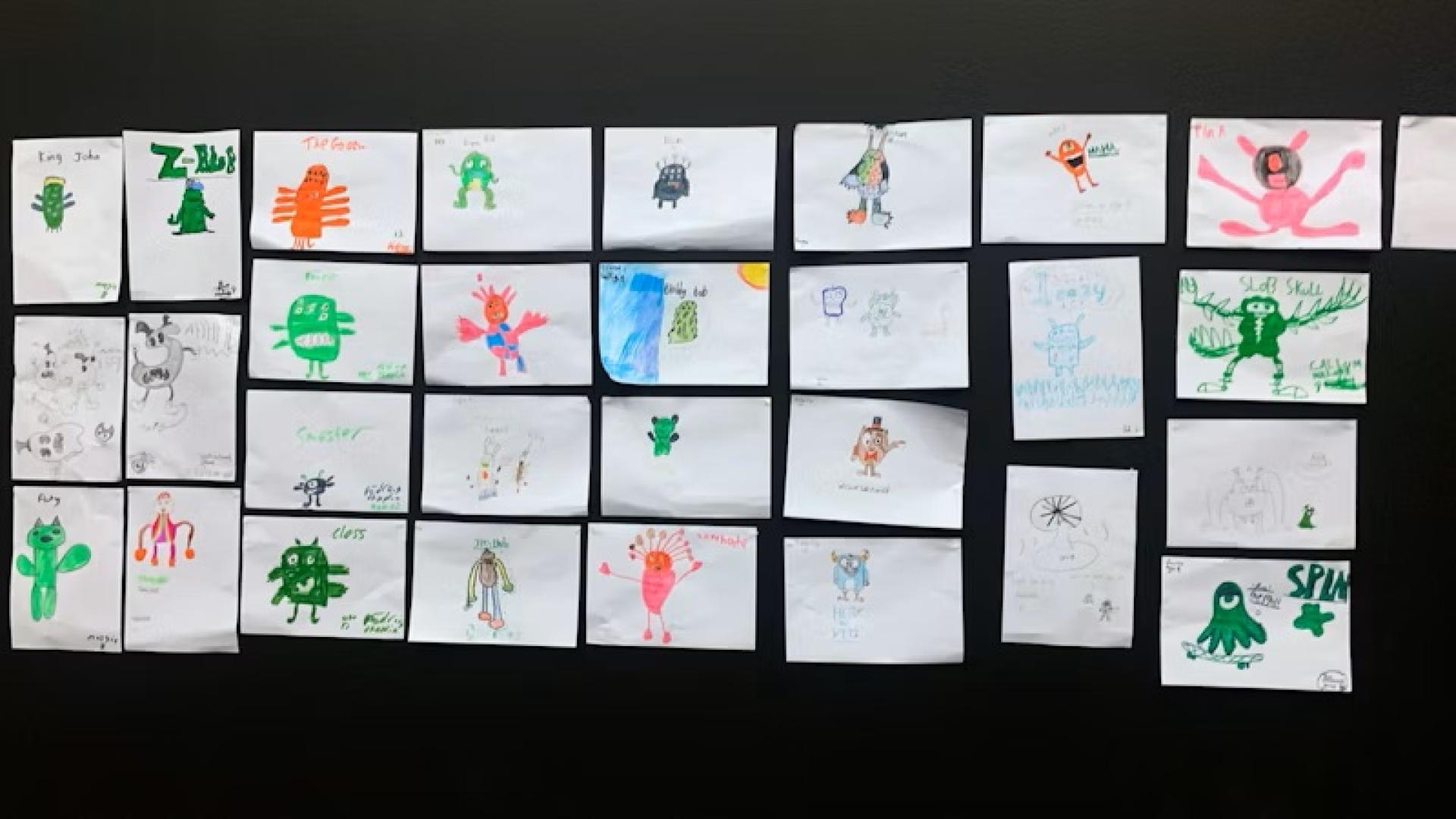 Wall display of multiple children’s monster drawings arranged in rows.