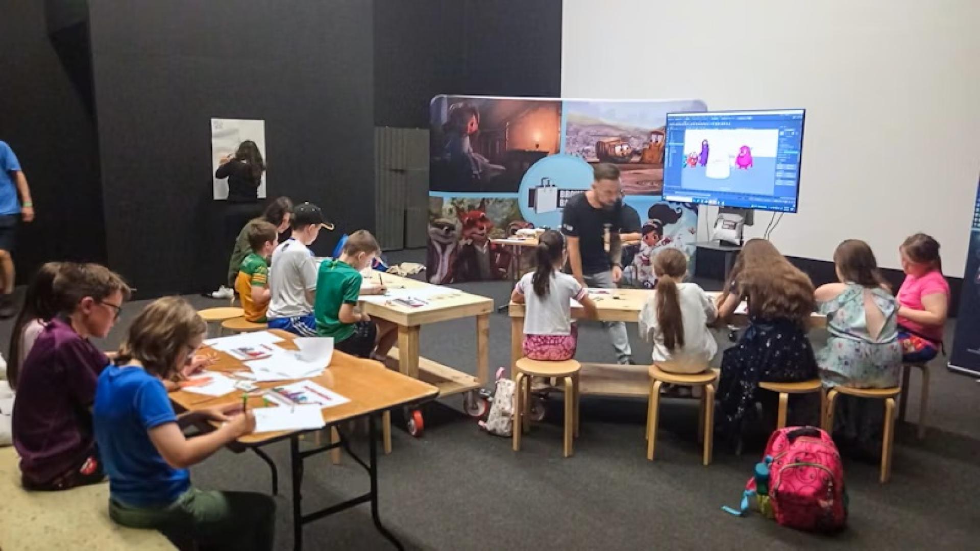 Children seated at tables during an animation workshop, drawing and coloring monster designs.