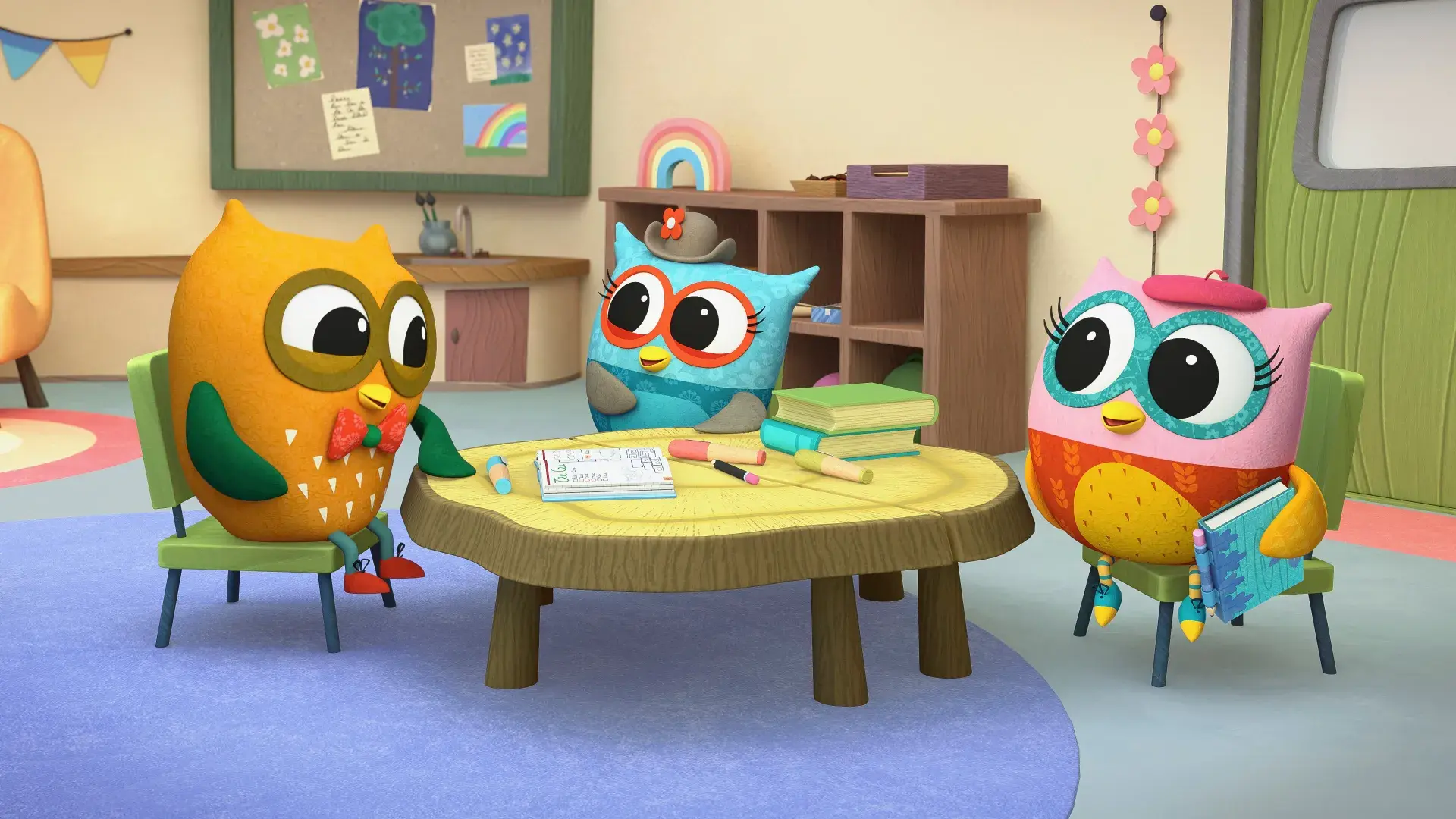 Three colorful owl characters sitting around a wooden table with books and pencils in a cozy classroom setting.