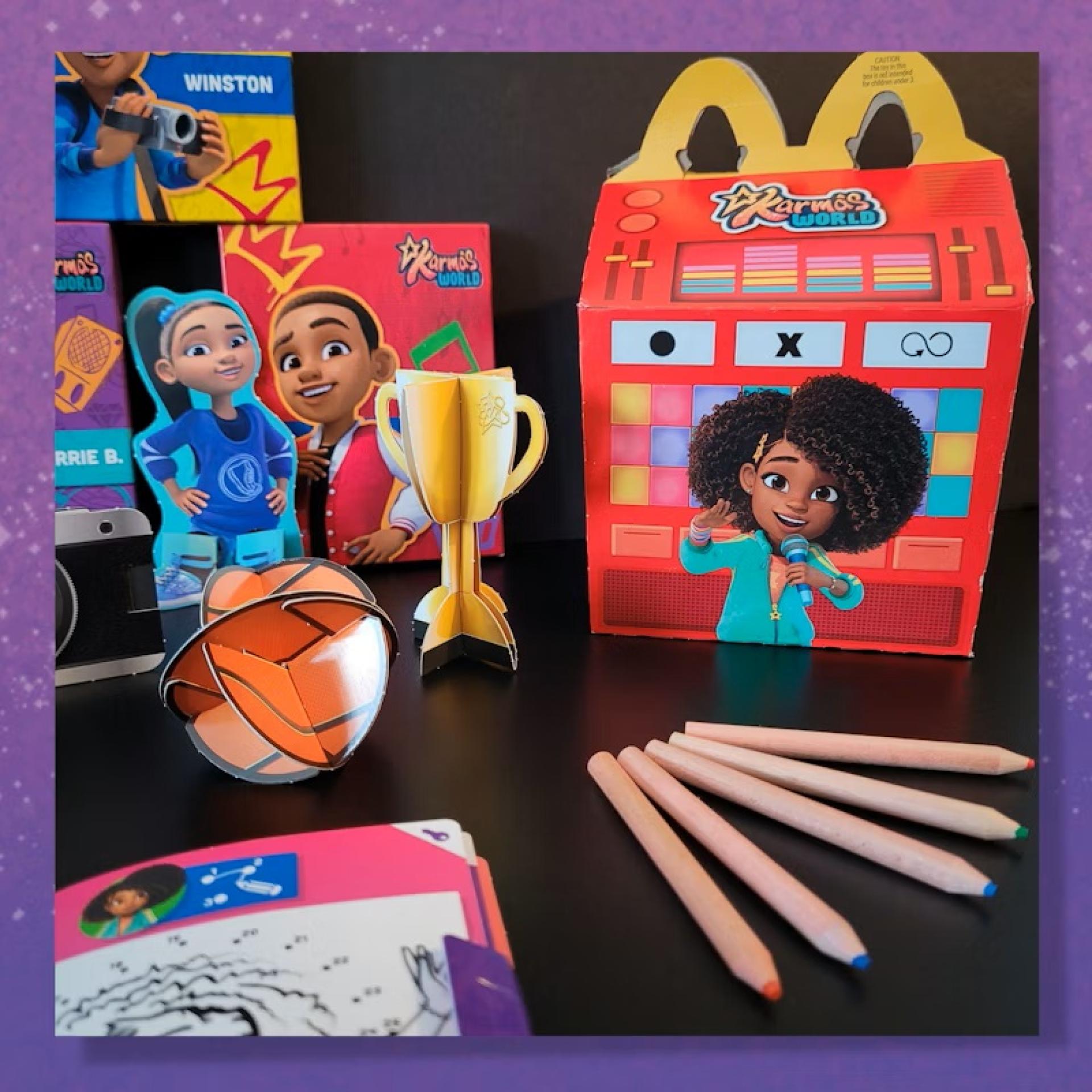 Karma’s World Happy Meal box with character cutouts, trophy, basketball, colored pencils, and activity sheets arranged on a table.