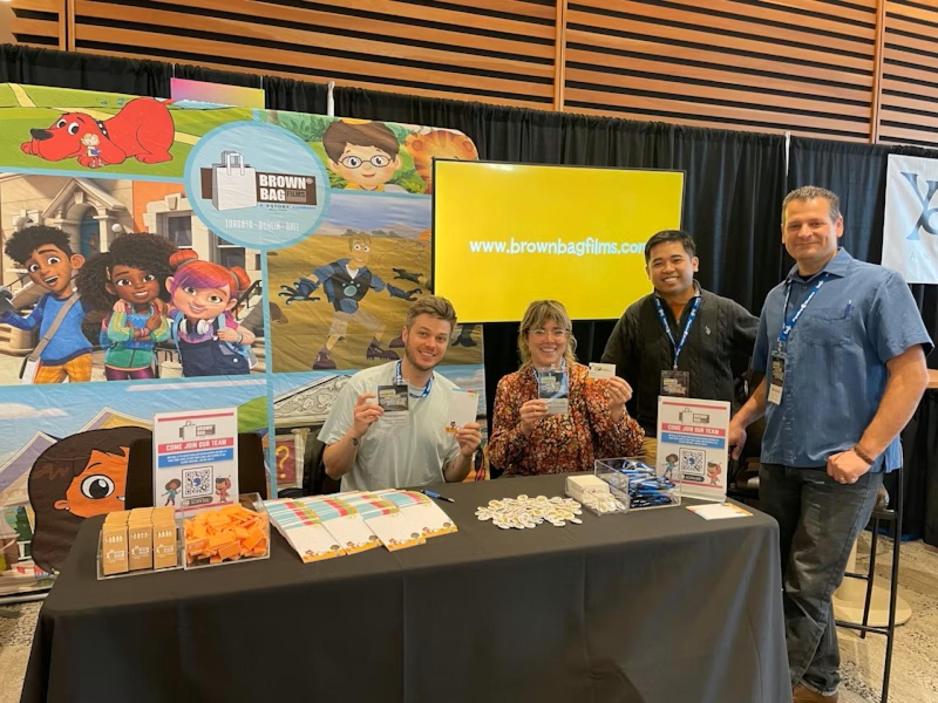 Brown Bag Films booth display featuring colorful character banners, branded signage, and giveaway items on the table.