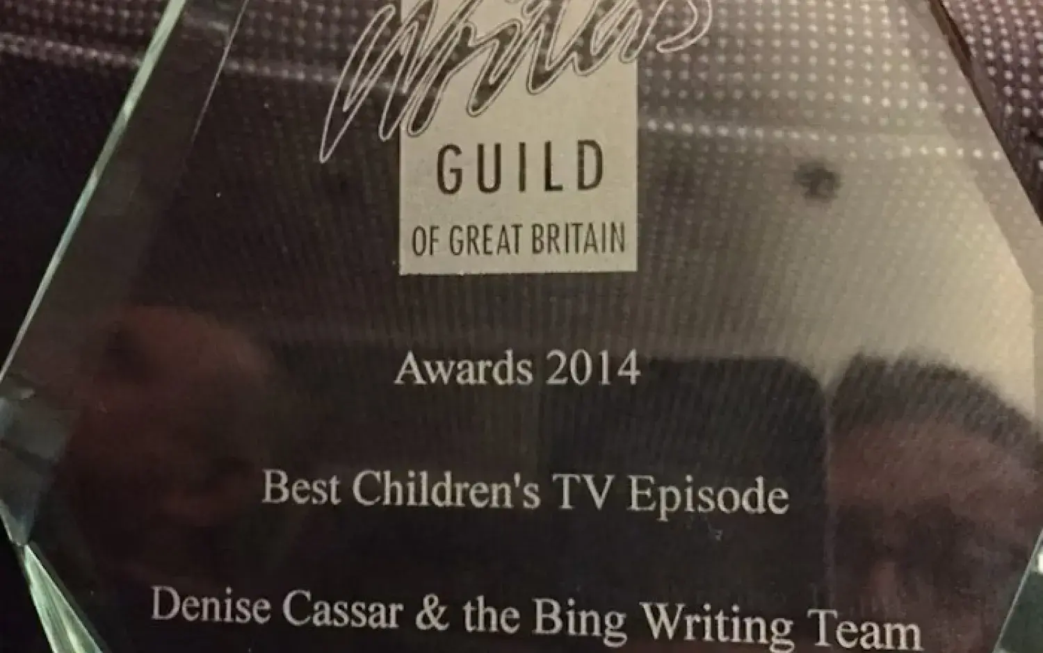A glass award plaque from The Writers' Guild of Great Britain recognizing “Best Children's TV Episode” in 2014 for “Bing: Bye Bye” by Denise Cassar and the Bing writing team.