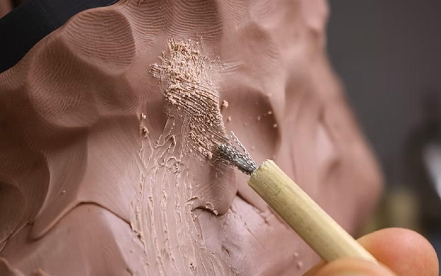 Close-up of a sculpting brush smoothing textured clay surface.
