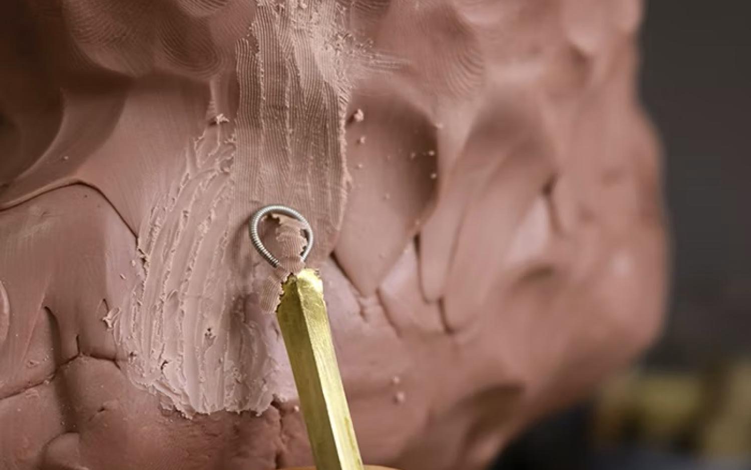 Wire loop tool creating grooves and texture on clay sculpture.