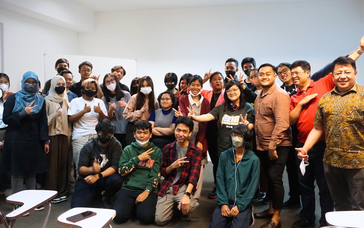 Large group photo of students and presenters posing together in a classroom setting.