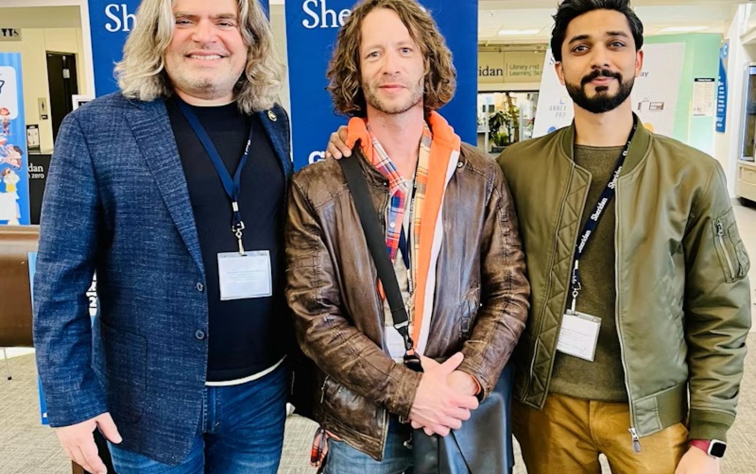 Three people standing indoors wearing event badges in front of Sheridan banners.