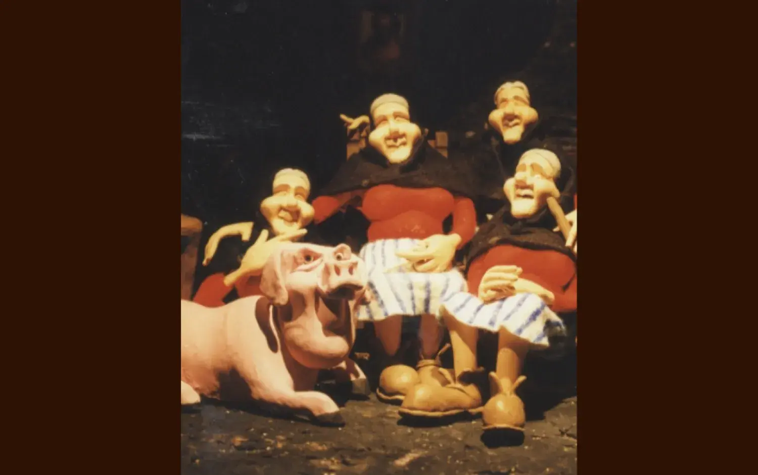 Stop-motion set featuring clay figures of four seated models of Peig Sayers and a pig in front of a dark backdrop.