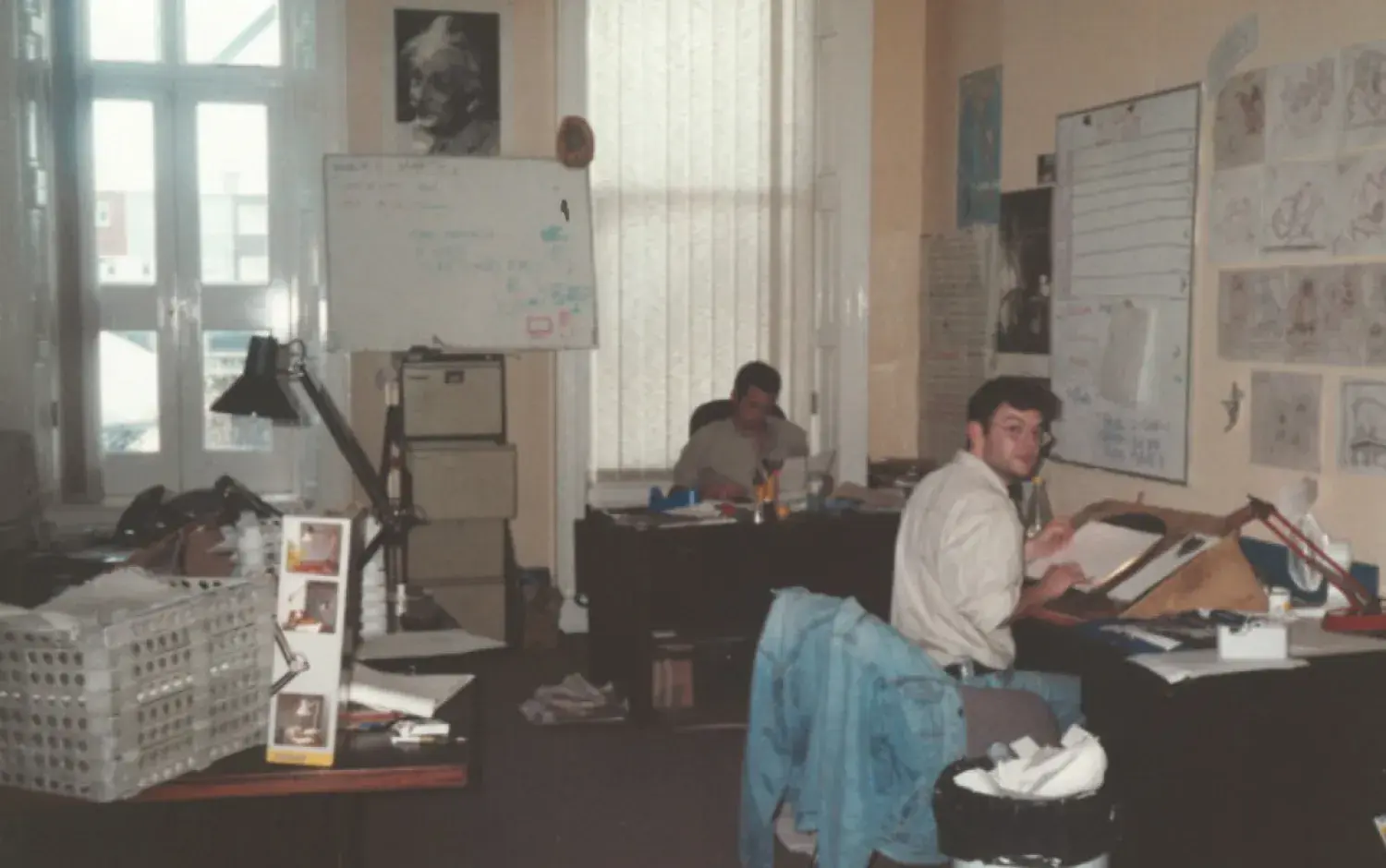 Animation studio room with two people at desks, a whiteboard, and walls covered in drawings and notes.