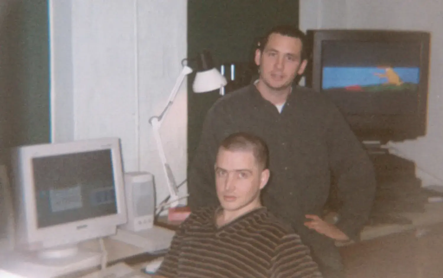 Two people in a studio with a computer and a TV screen displaying colorful animation.