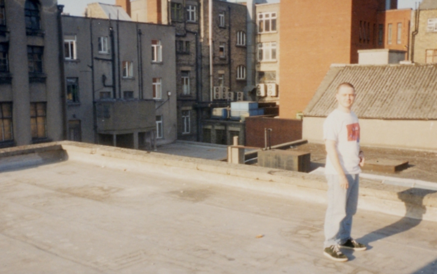 Person standing on a rooftop surrounded by older brick buildings and urban architecture.