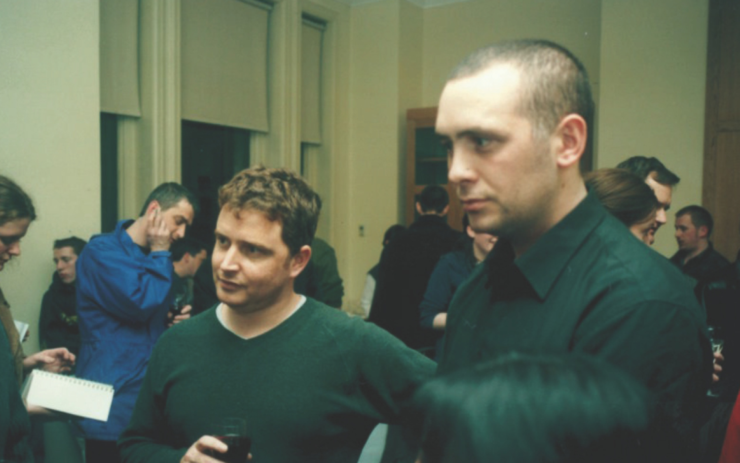 Group of people gathered in a room during a social event, some holding drinks and chatting.