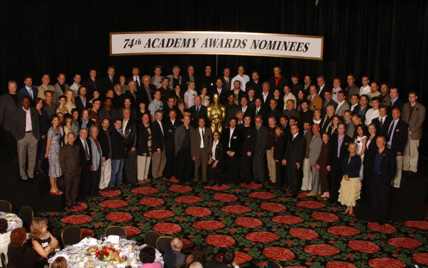 Large group photo of Academy Awards nominees posed on a stage with a golden Oscar statue and a banner reading “74th Academy Awards Nominees.”