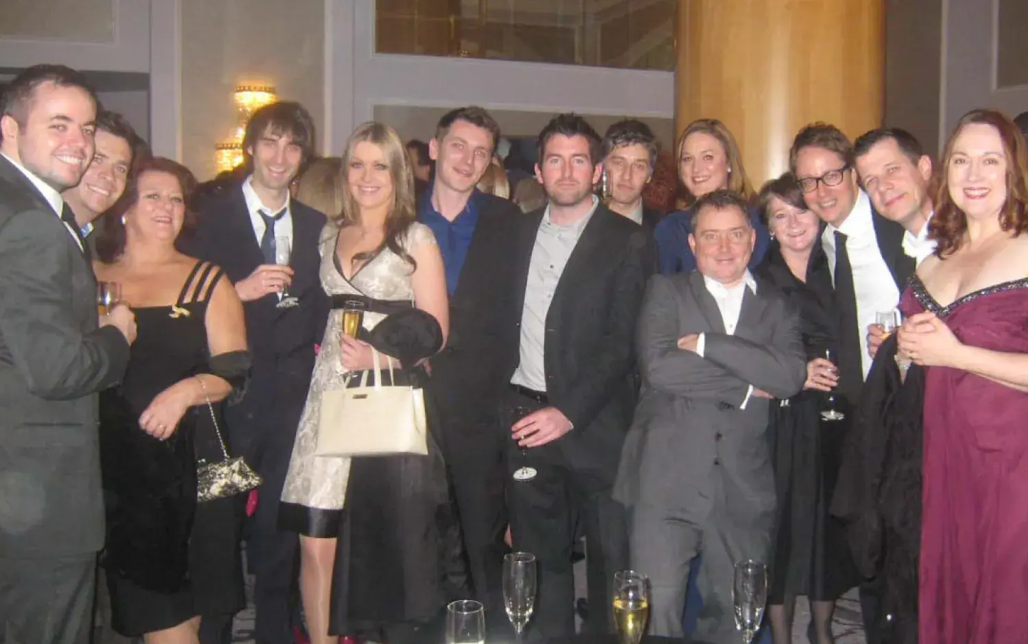 Large group of people in formal attire gathered at a reception, holding champagne glasses.
