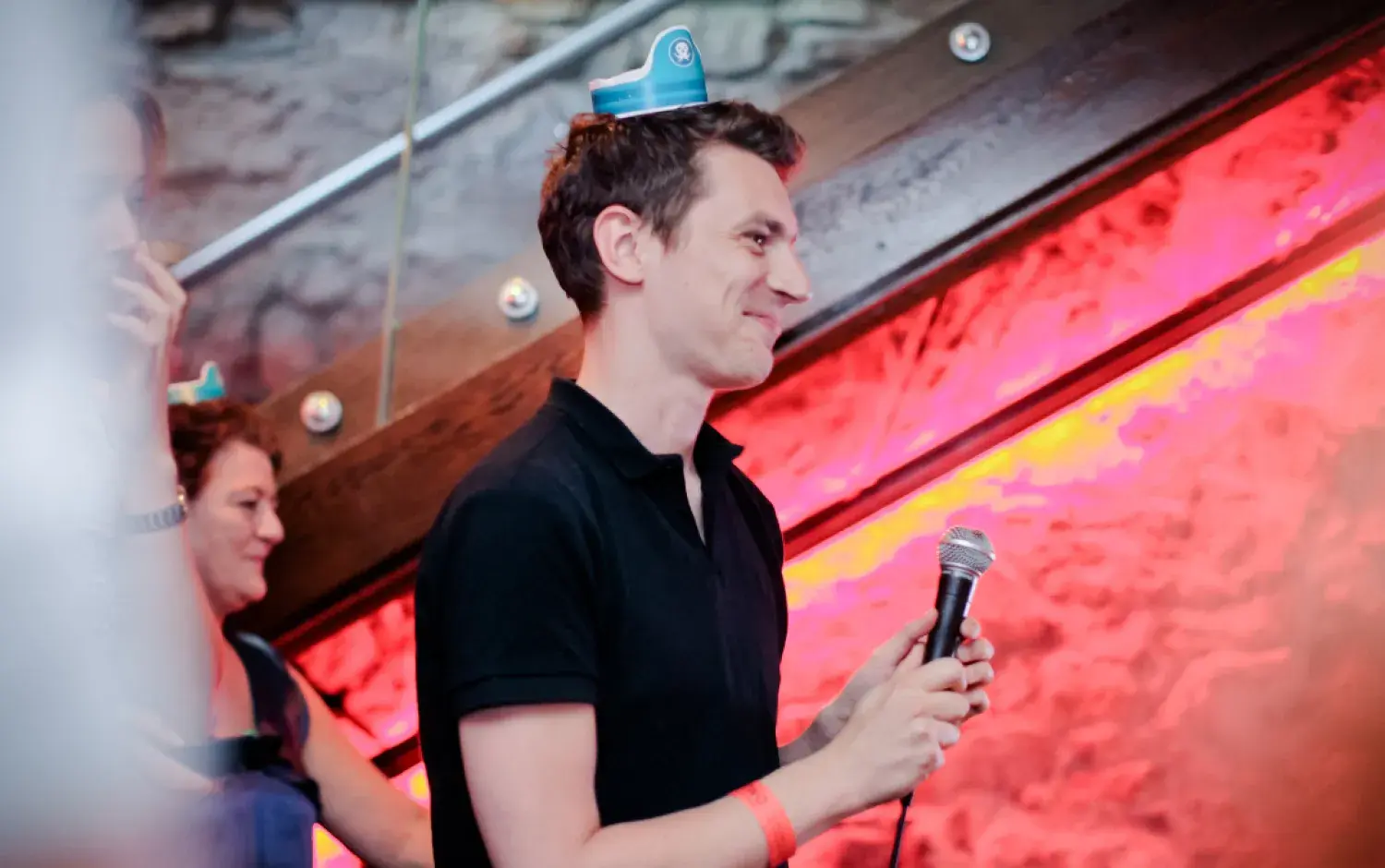 Person holding a microphone on a stage with red lighting and a stone wall background.