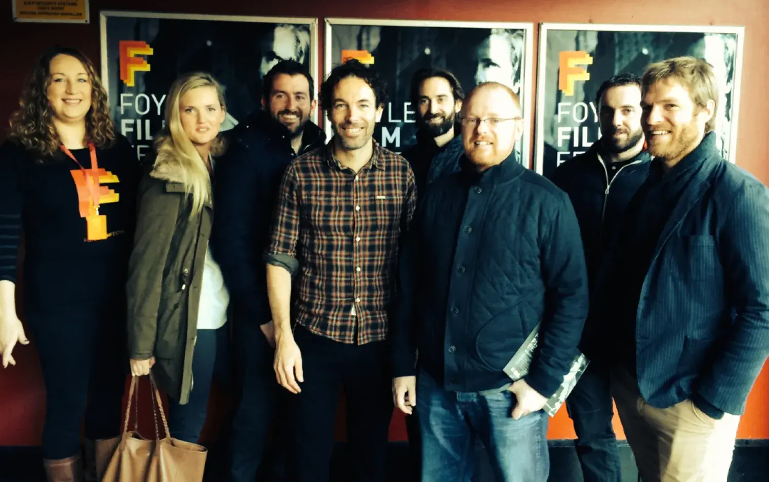 Group of people standing in front of Foyle Film Festival posters inside a venue.
