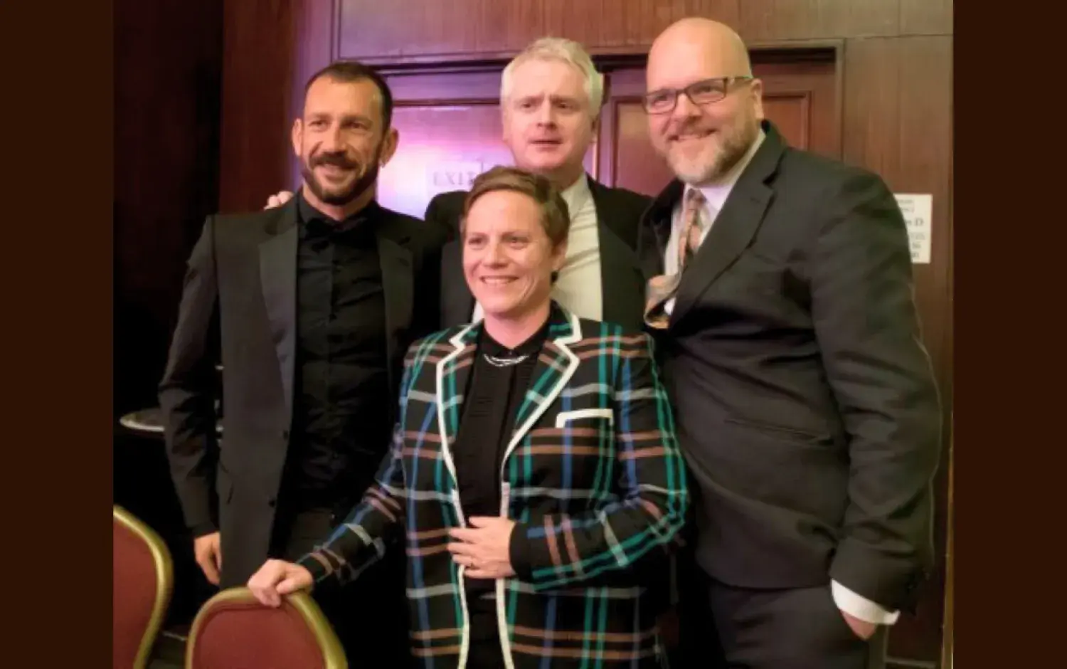 Group of four people posing indoors in formal attire.