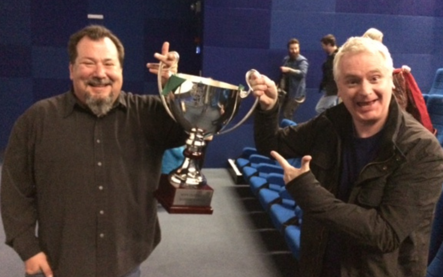 Two people standing in a theater holding a large silver trophy cup.