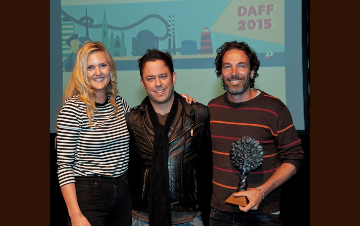 Three people standing in front of a DAFF 2015 backdrop, one holding a tree-shaped award.