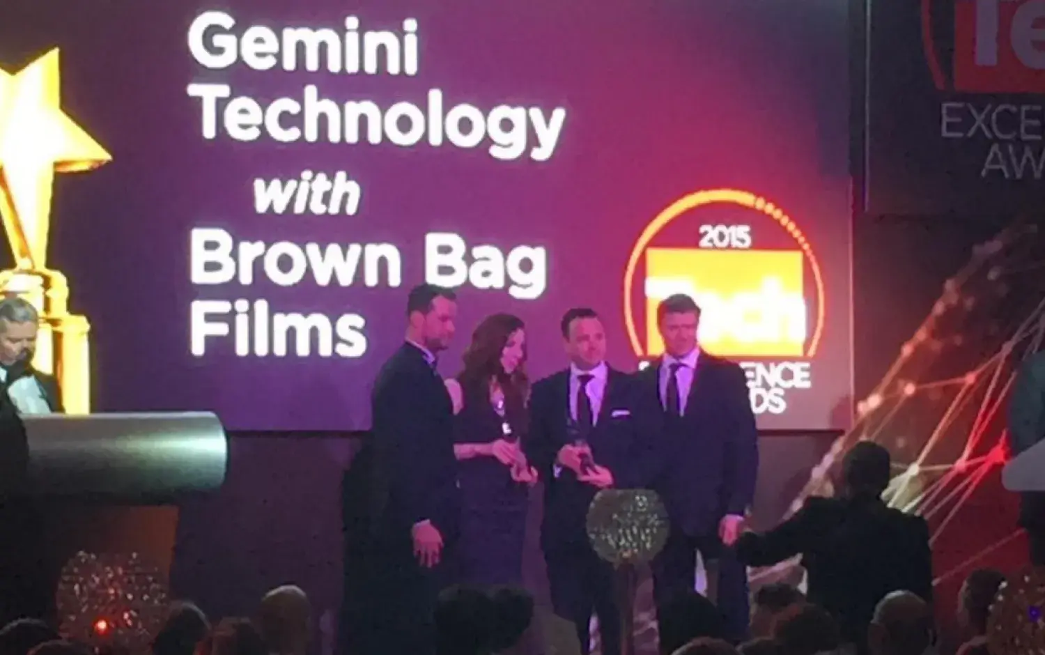 Group on stage at Tech Excellence Awards with screen displaying “Gemini Technology with Brown Bag Films.”