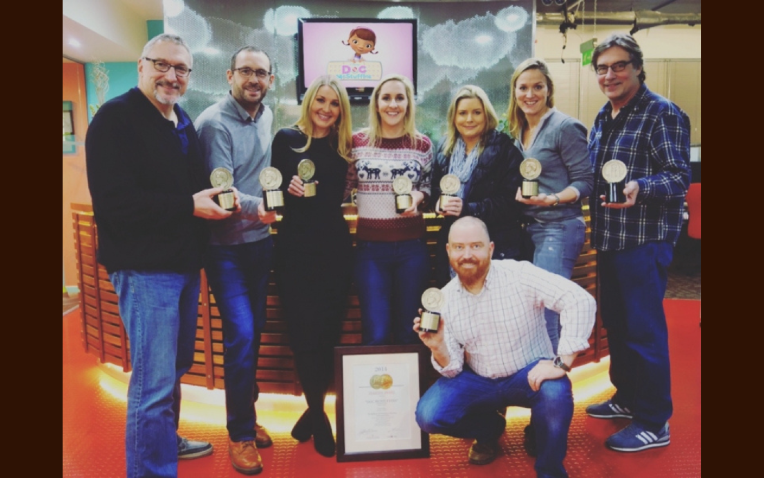 Group of eight people indoors holding multiple Peabody Award trophies and a framed certificate.