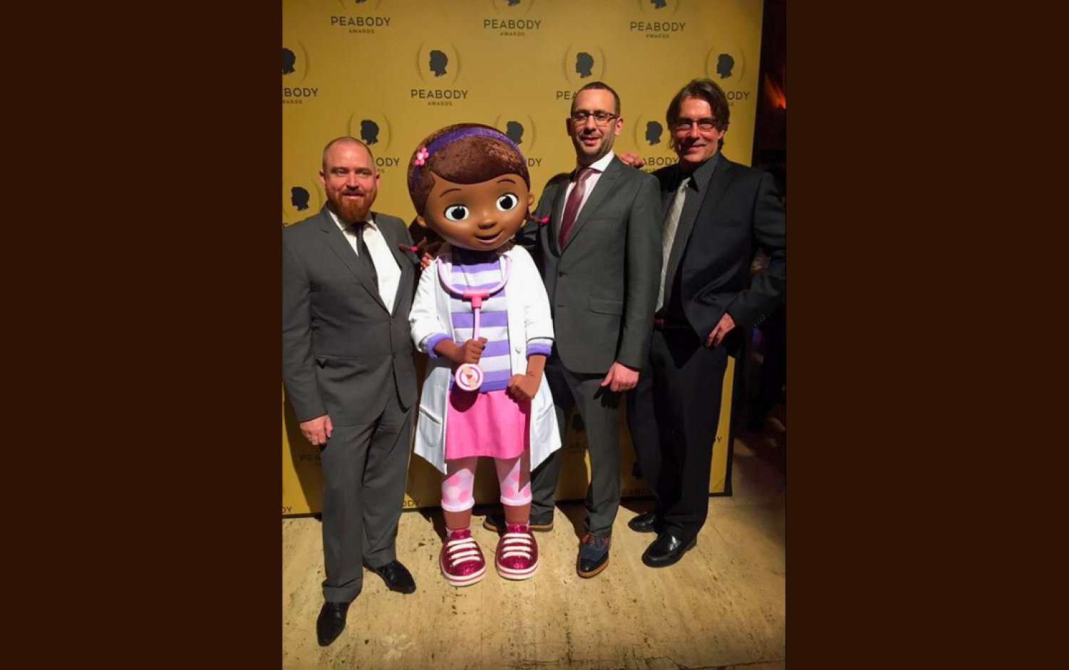 Group posing on Peabody Awards red carpet with a Doc McStuffins character mascot.