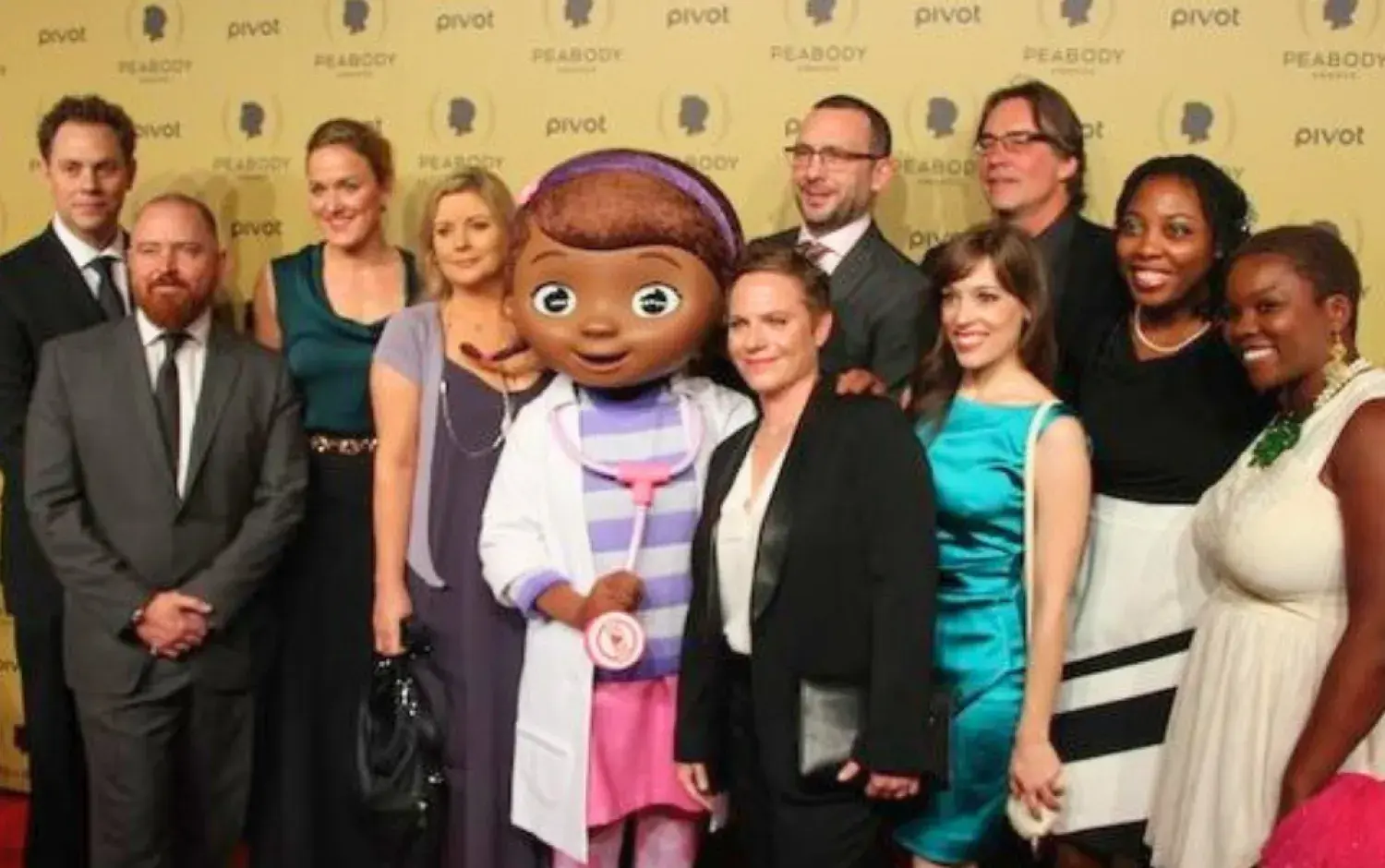 Group photo on Peabody Awards red carpet with mascot in center.