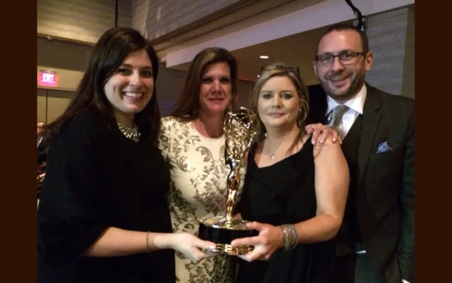 Group holding an Emmy Award trophy together at an indoor ceremony.