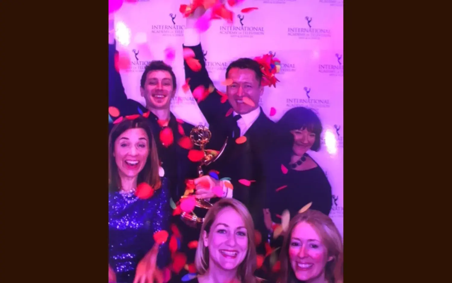 Celebratory photo with rose petals falling and an Emmy Award held high.
