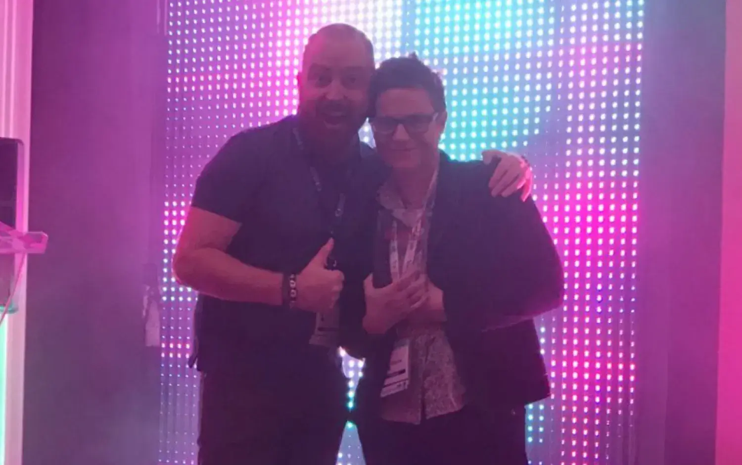 Two people standing in front of a colorful LED backdrop at an event stage.