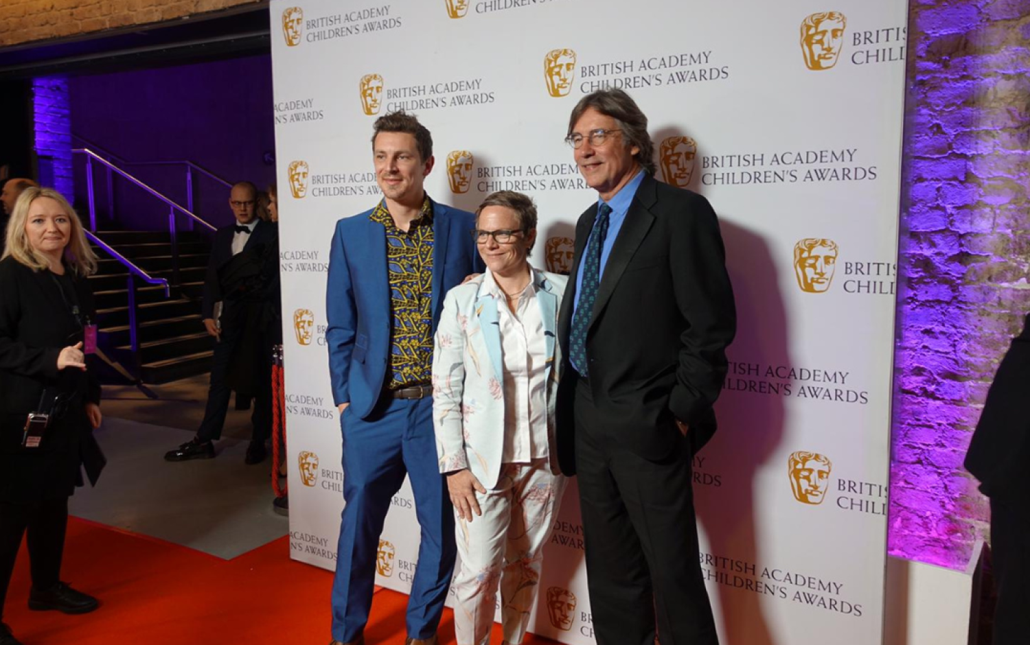 Three people posing on the red carpet in front of a British Academy Children’s Awards backdrop.