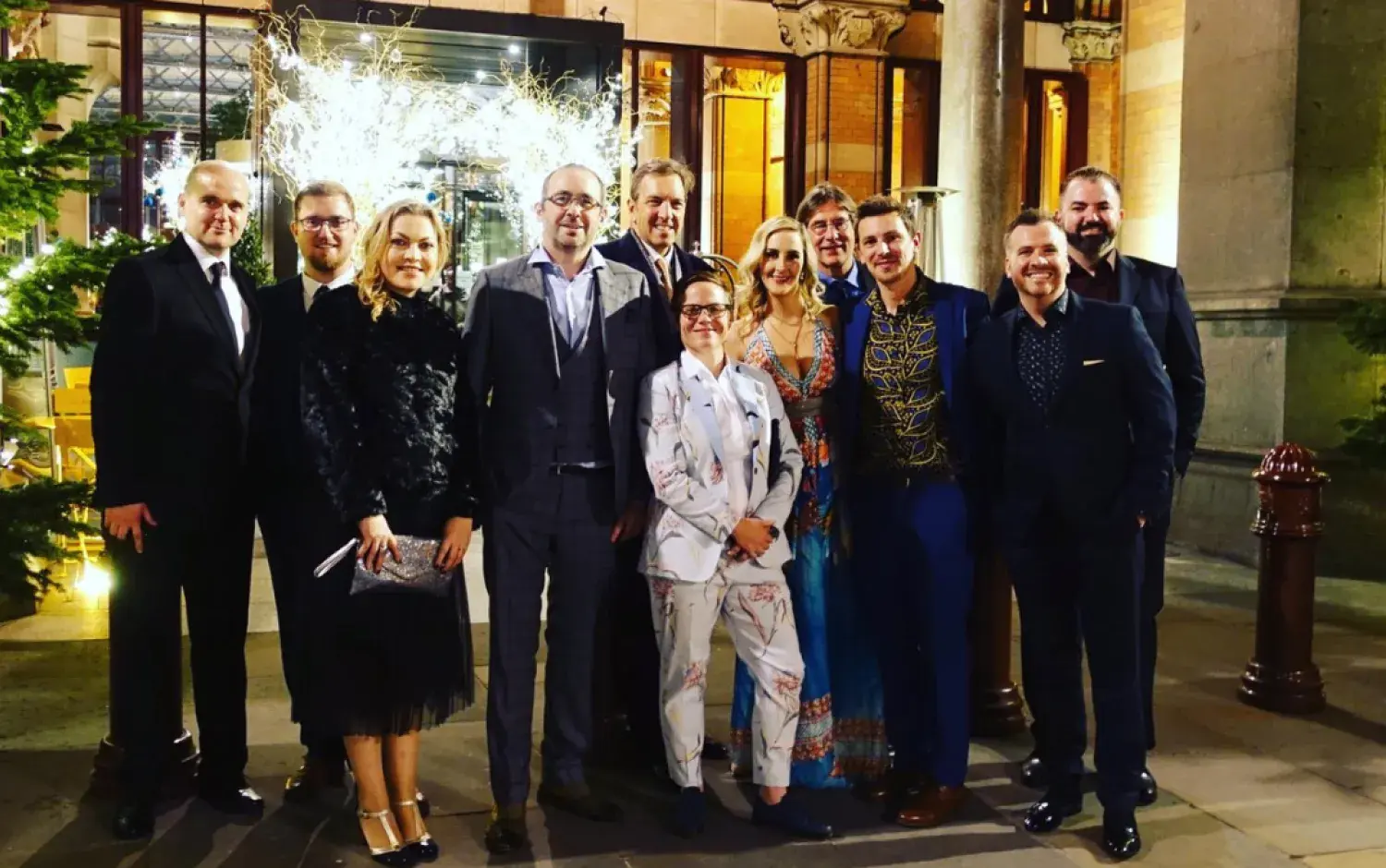 Group standing outside a building decorated with festive lights and greenery.