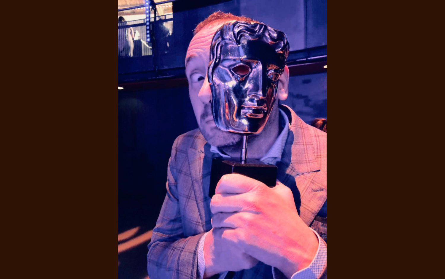 Cathal Gaffney holding a BAFTA award statuette in front of his face at the awards ceremony.