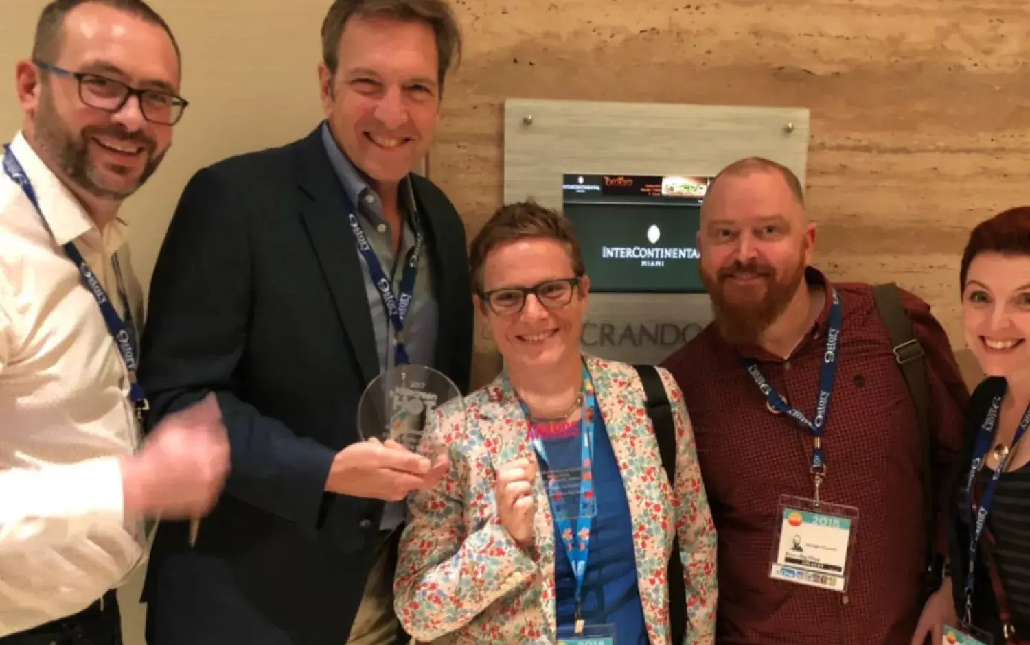 People posing indoors holding a clear circular award.