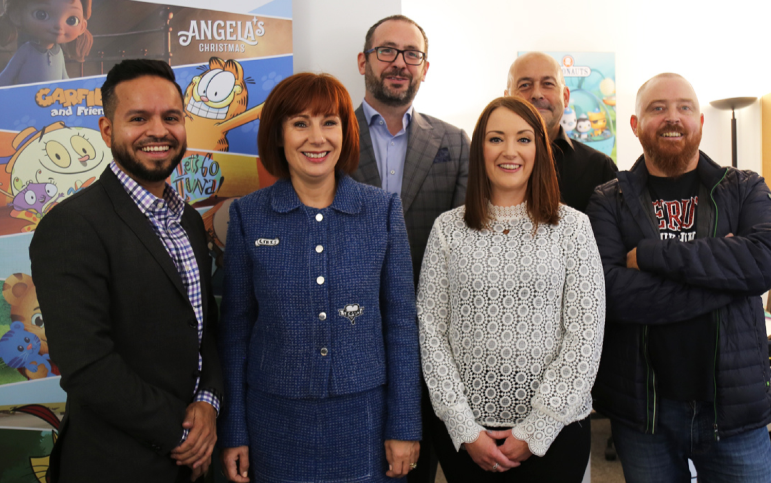 Group posing in front of colorful posters featuring animated characters.
