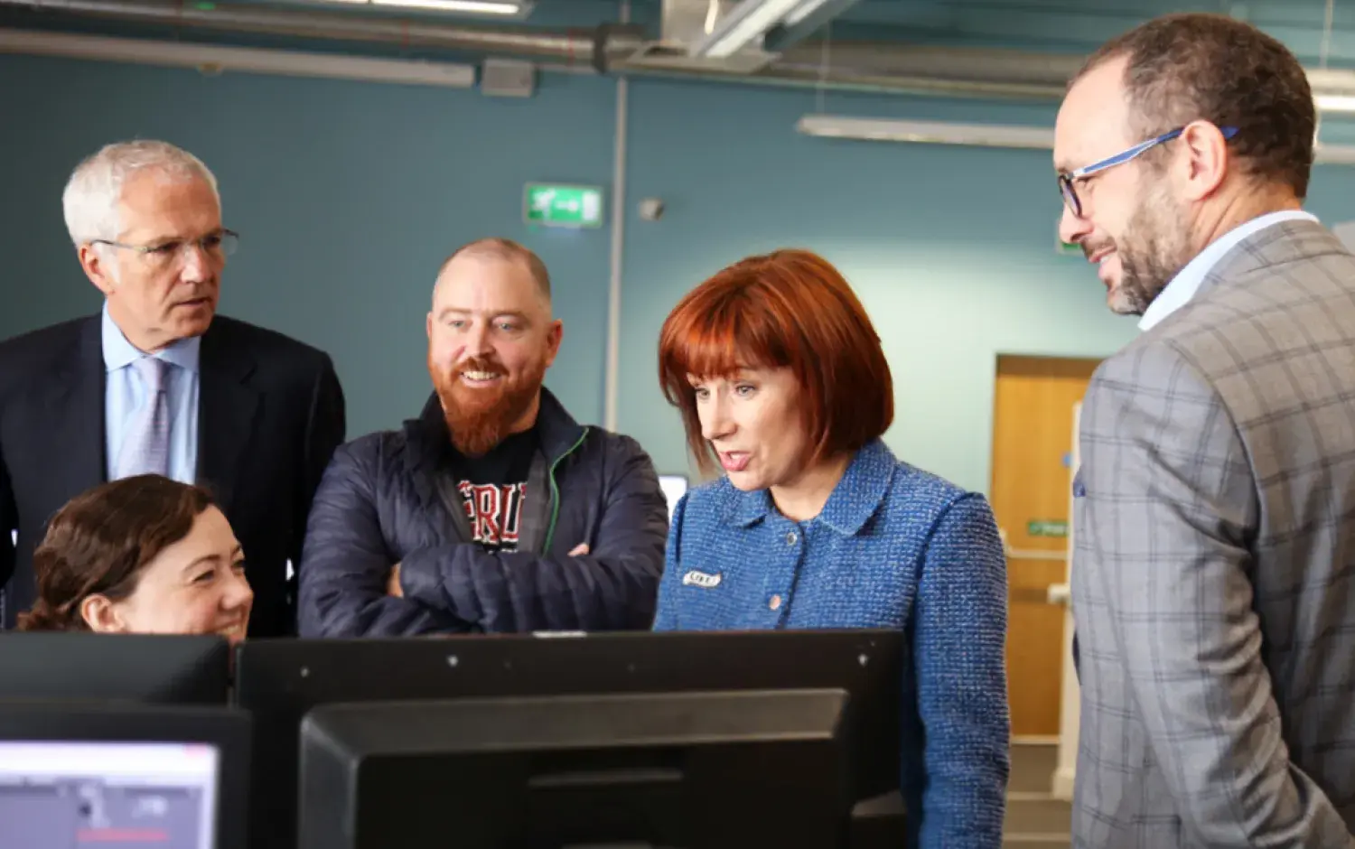 Individuals observing computer screens in an open-plan office environment.