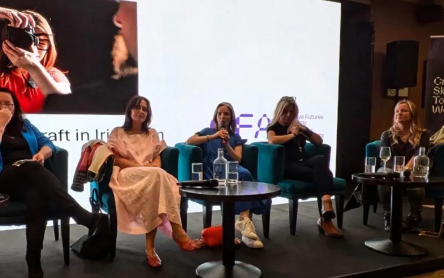 Panel of five speakers seated on stage in front of a large presentation screen during a conference.