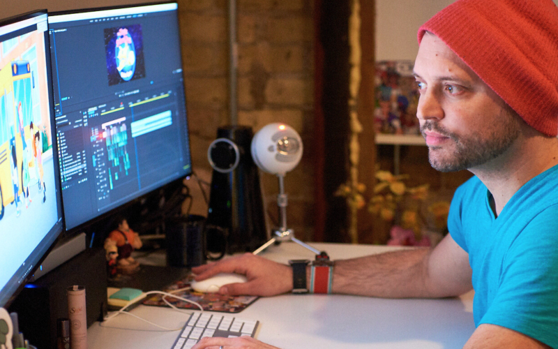 A person working alone at a desk with two monitors, one displaying animation software.