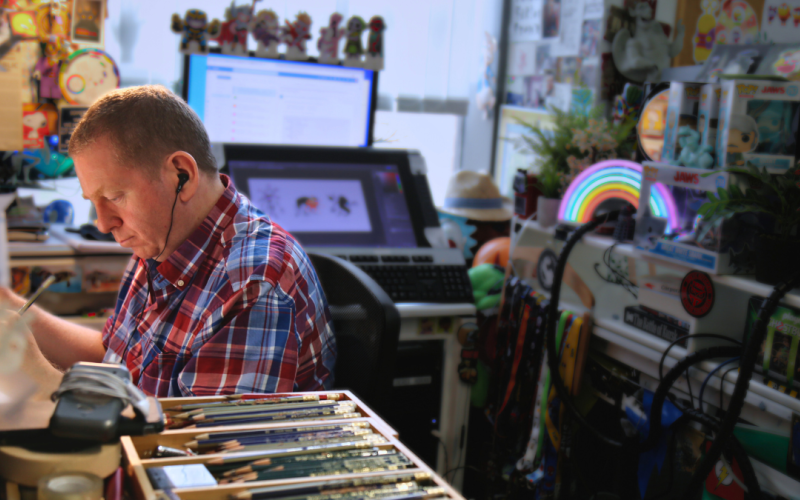 Person working at a toy cluttered desk with various drawing tools and equipment.