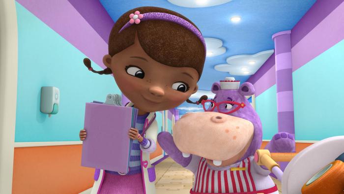 Doc McStuffins holding a clip board walking down the Toy Hospital hallway with Hallie