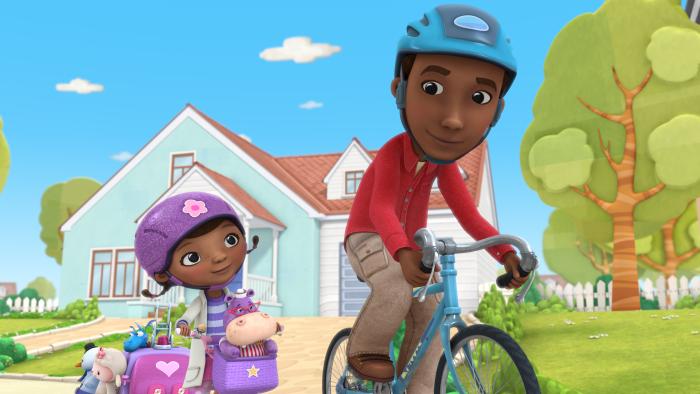 Doc McStuffins and her dad cycling. Doc is wearing a purple helmet and has Hallie in her bike basket. Her dad is wearing a blue helmet.
